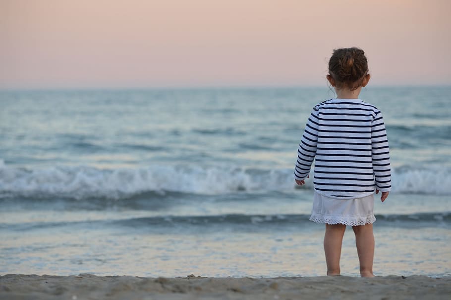 A child baby looking out to the ocean on the beach, people, children