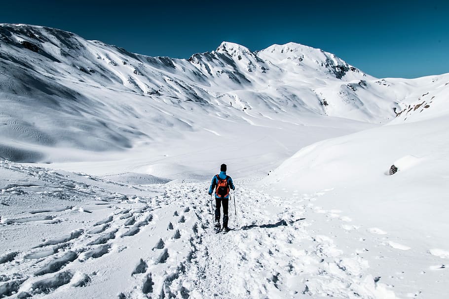 man walking on snow field near mountain, person snow skiing beside mountain during day time HD wallpaper
