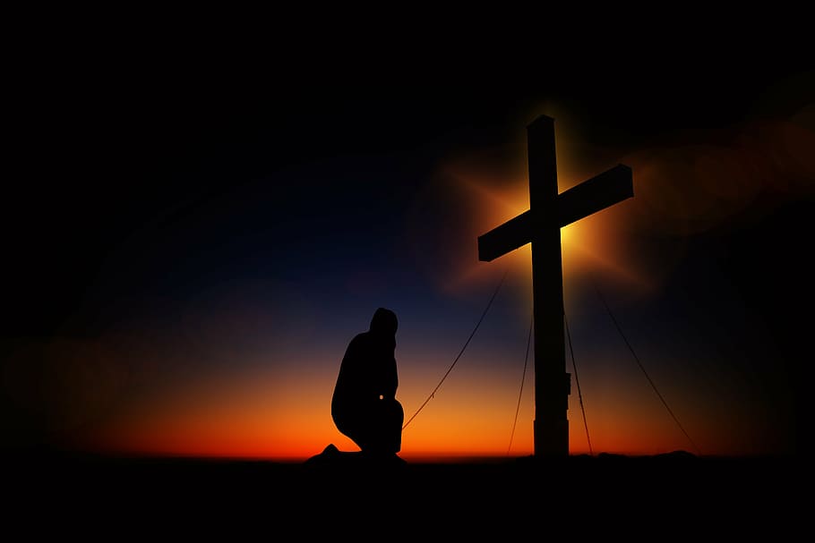 silhouette of man kneeling in front of a cross, sunset, humility