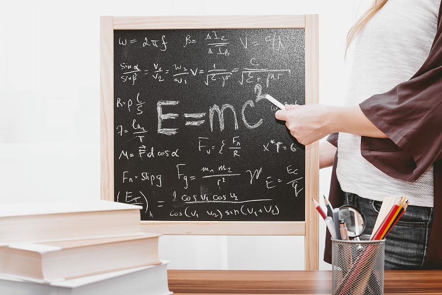 E-mc2 written on chalkboard, woman writing mathematical equations on blackboard using chalk