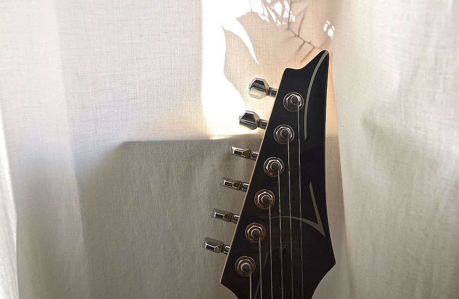 black guitar headstock near white curtain, electric guitar, stringed instrument