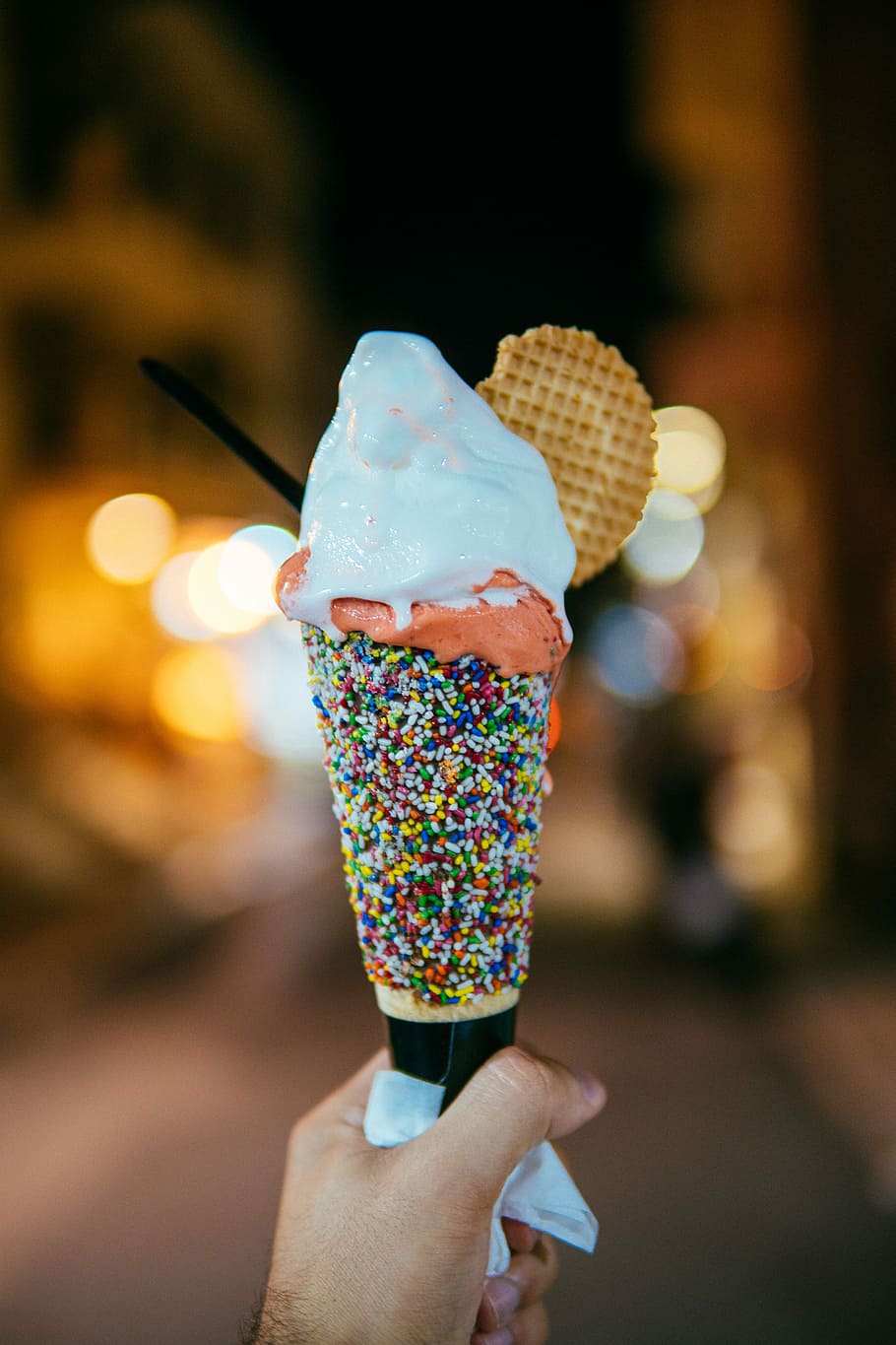 person holding multicolored sprinkled ice cream cone with vanilla flavored ice cream, focused photo of a white ice cream with cone
