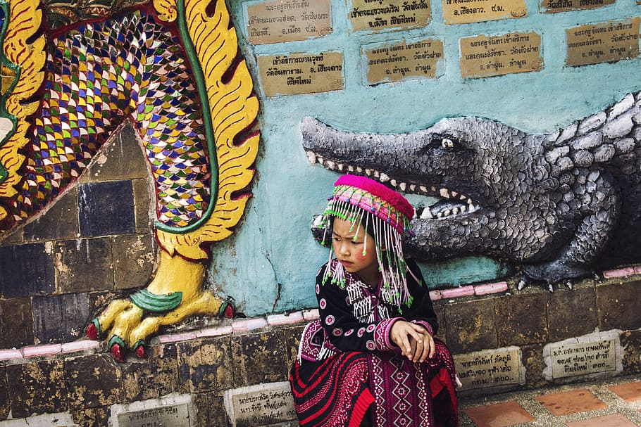 girl wearing multicolored traditional dress sitting near the wall, girl sitting near painted wall taken during daytime