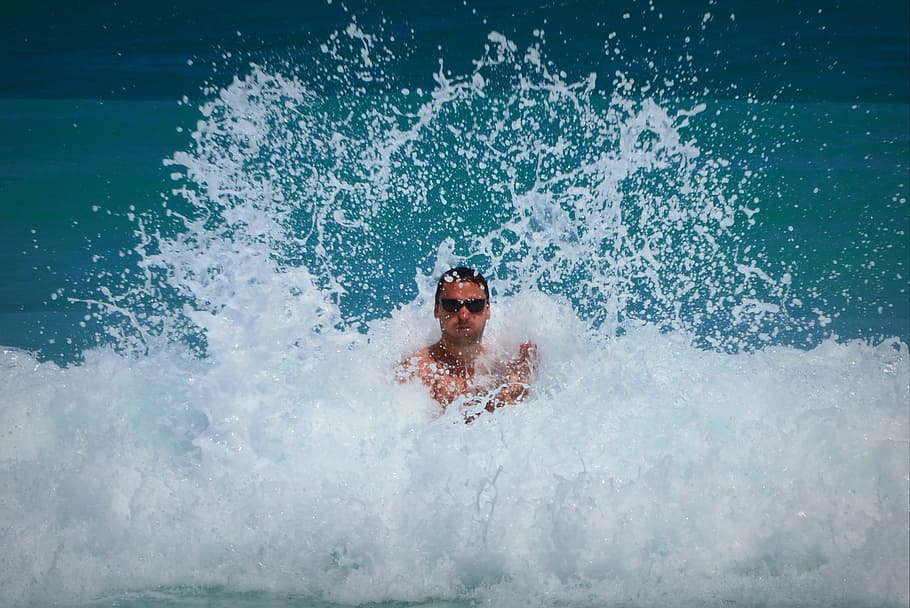 man wearing sunglasses standing between sea waves during daytime HD wallpaper