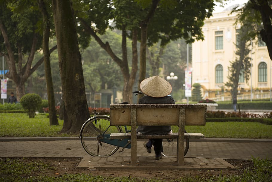 person sitting on bench in front of commuter bike, person wearing hat sitting on brown bench near tree HD wallpaper