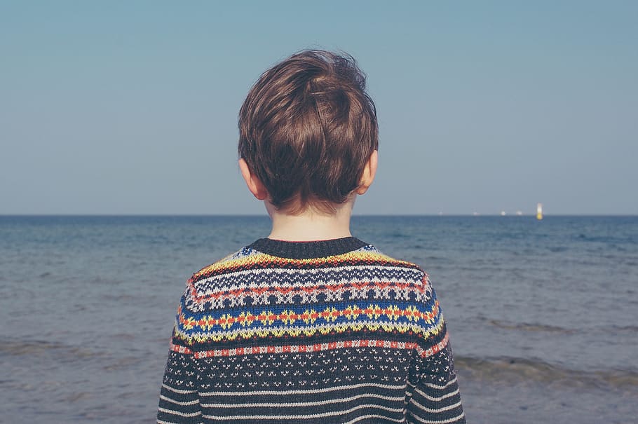 person wearing multicolored striped floral sweater facing the sea, boy standing beside sea HD wallpaper