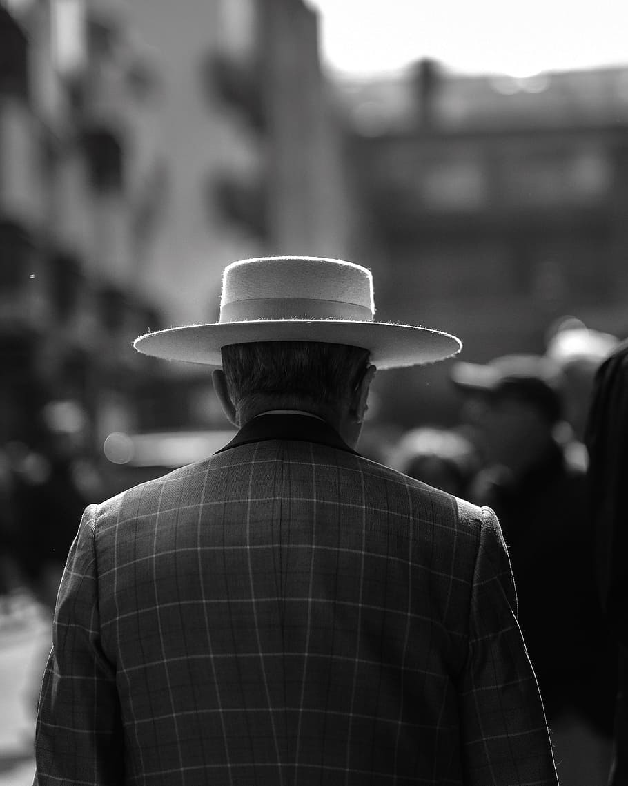 grayscale photo of man wearing hat standing beside building, greyscale photo of man wearing hat near people HD wallpaper