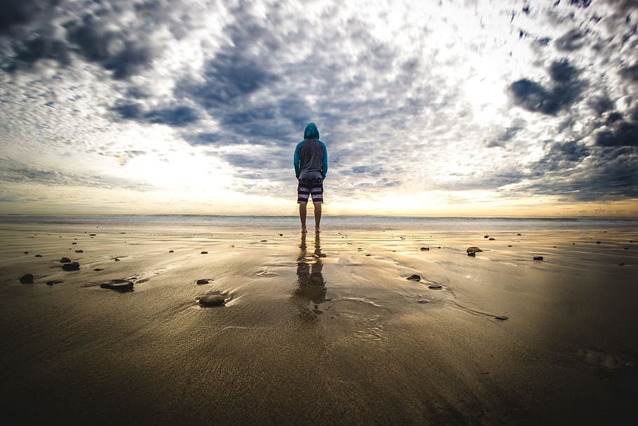 man in hoodie jacket standing near shoreline, person standing on sand HD wallpaper