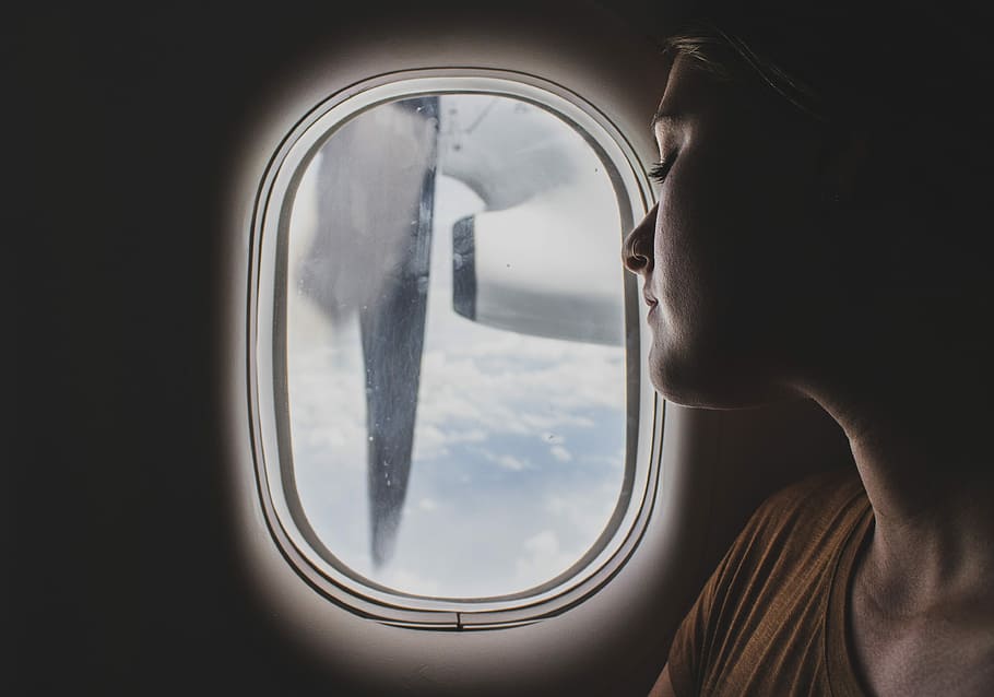 woman wearing brown scoop-neck sitting near airplane window while sleeping during flight, woman looking outside airliner window
