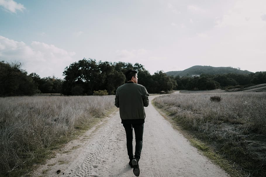 man walking on empty road, man walking between grass field during daytime HD wallpaper