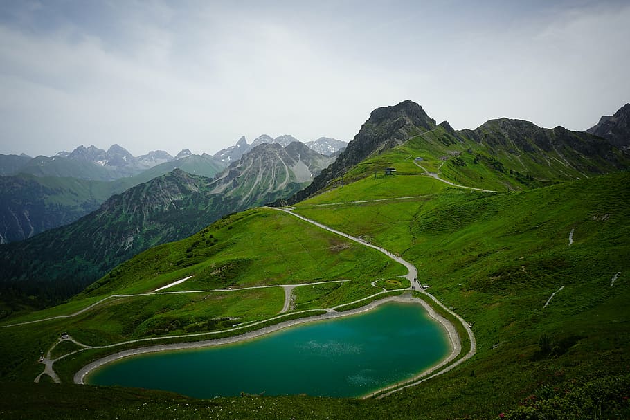 green mountain range with blue body of water under cloudy skies HD wallpaper