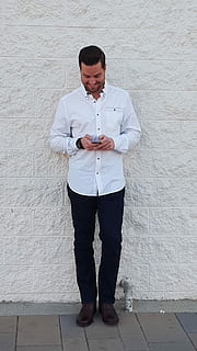 man using smartphone while standing against the white wall HD wallpaper