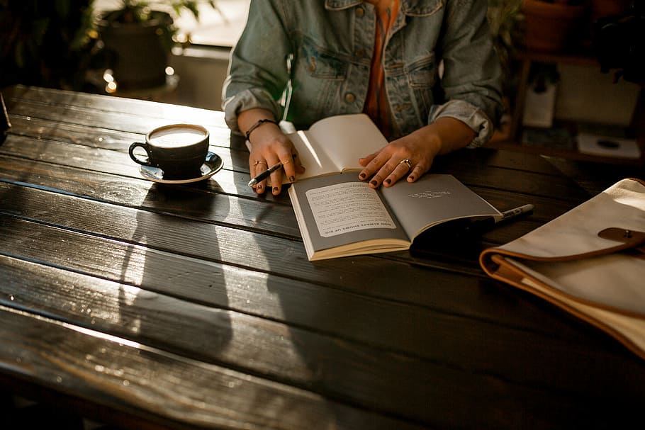 person opening notebook on brown wooden table, woman reading a book while having a coffee HD wallpaper
