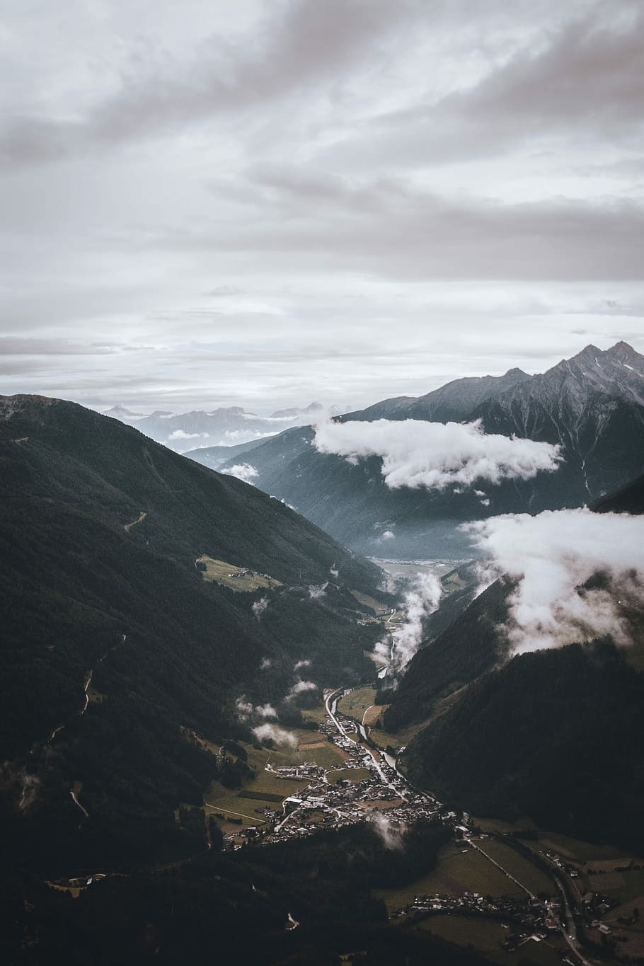bird's eye view of city surrounded by mountains, aerial photography of buildings below mountains under gray sky HD wallpaper