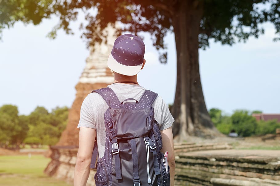 man wearing gray backpack standing near tree at daytime, people