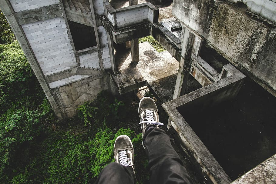 human wearing black pants and pair of gray Vans Old Skool sitting on cliff of abandoned concrete house HD wallpaper