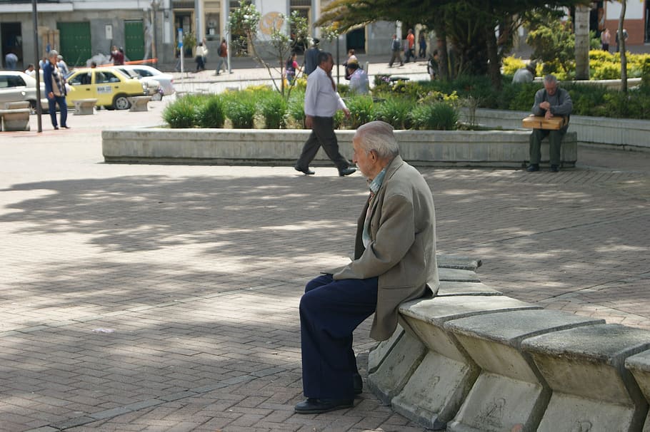 shallow focus photography of man in gray formal suit jacket sitting on gray concrete bench during daytime