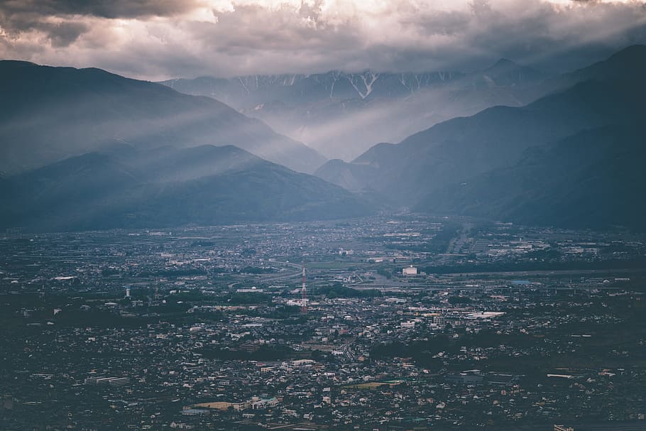 aerial view of city at daytime, aerial photo of houses near silhouette of mountain under gray clouds with sun rays HD wallpaper