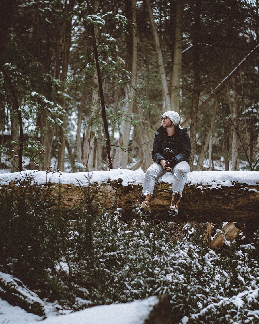 man wearing white knit cap and black jacket sitting on snow covered tree log, man sitting on tree trunk HD wallpaper