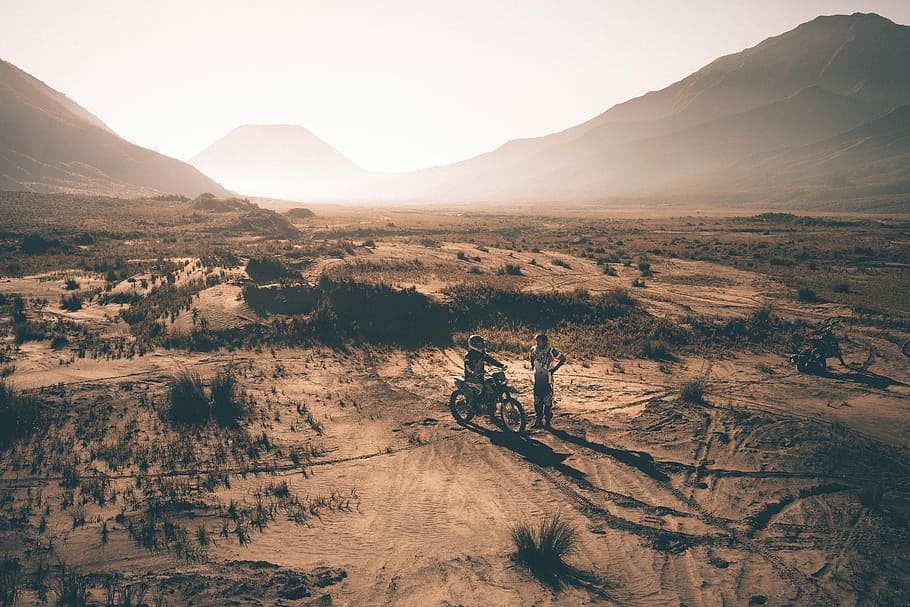 two person on motorcycle on rural land, two people on desert with dirt bike photo taken during golden hour HD wallpaper