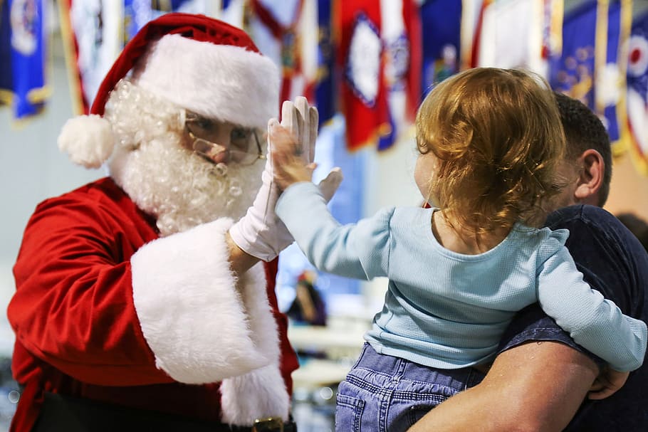 Santa Claus doing high five with girl carried by man during daytime