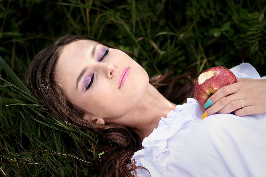 woman holding bitten apple lying on green grass, snow white, march