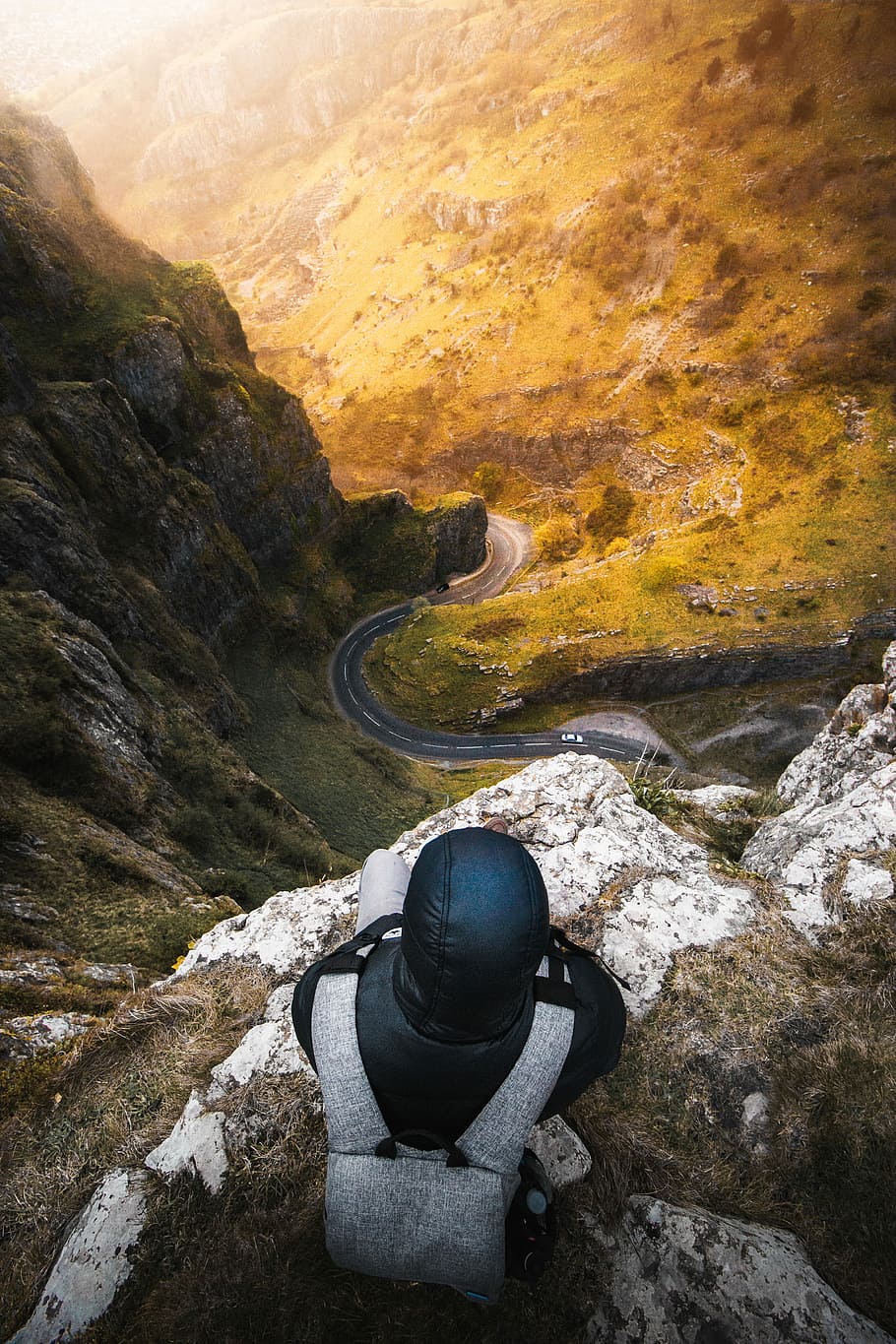 The best views, man sitting on edge of cliff looking down, road