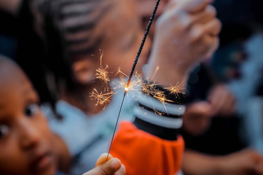 person holding sparkler beside boy, selective focus photo of person holding gray sparkler HD wallpaper