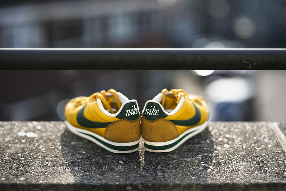 selective focus photography of yellow-black-and-white Nike Cortez shoes, pair of yellow-and-green Nike low-top sneakers on gray surface selective focus photography