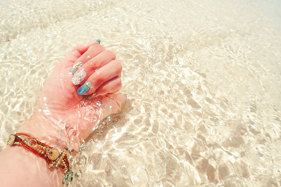 person hands  wearing gold bracelet and white-blue nail polish on body of water