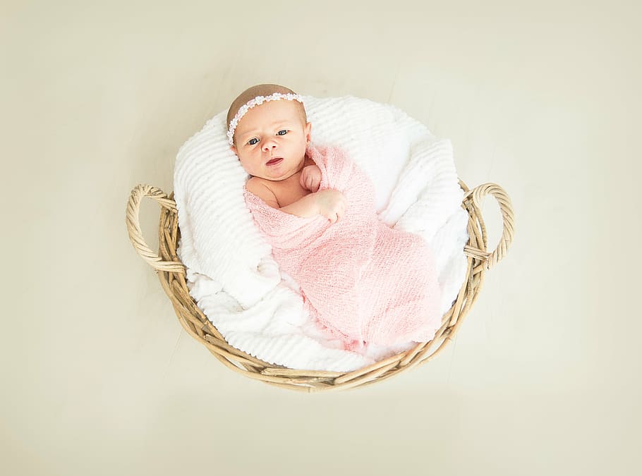 baby covered by pink swaddle on round brown wicker basket, girl