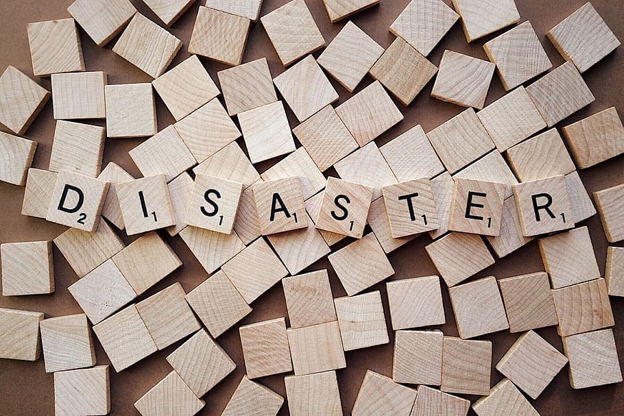 brown wooden scrabble tiles forming disaster word on top of other scrabble tiles HD wallpaper