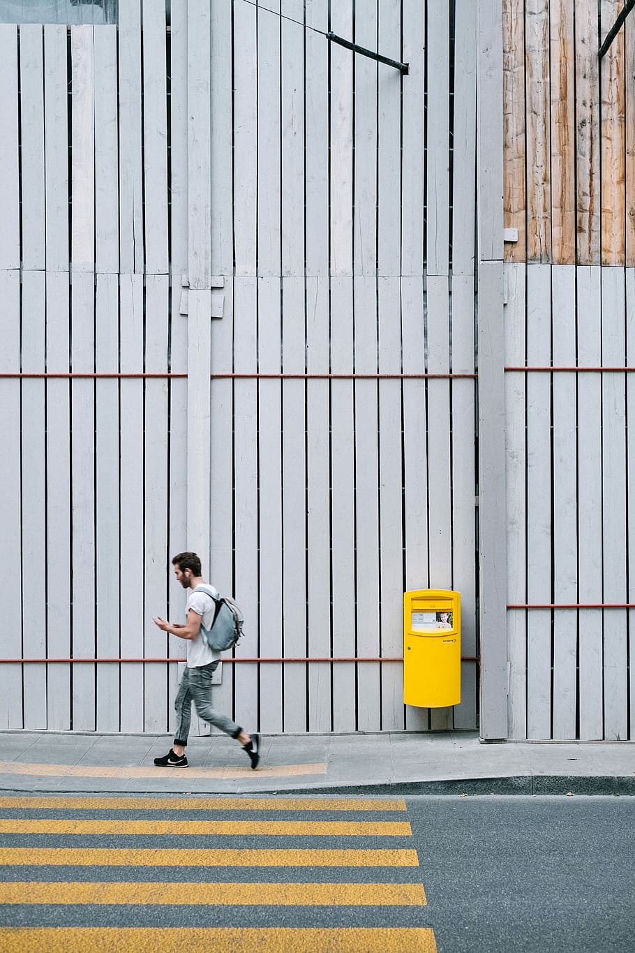 man walking on sidewalk beside tall gray wooden fence view from across the street photo HD wallpaper