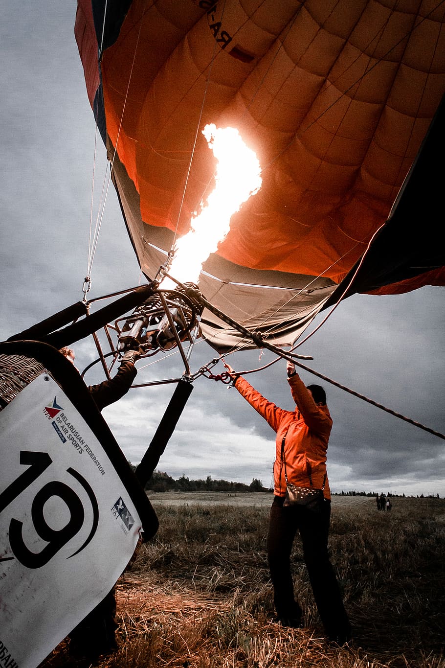 person arranging orange and black hot air balloon during daytime, man holding gray hot air balloon