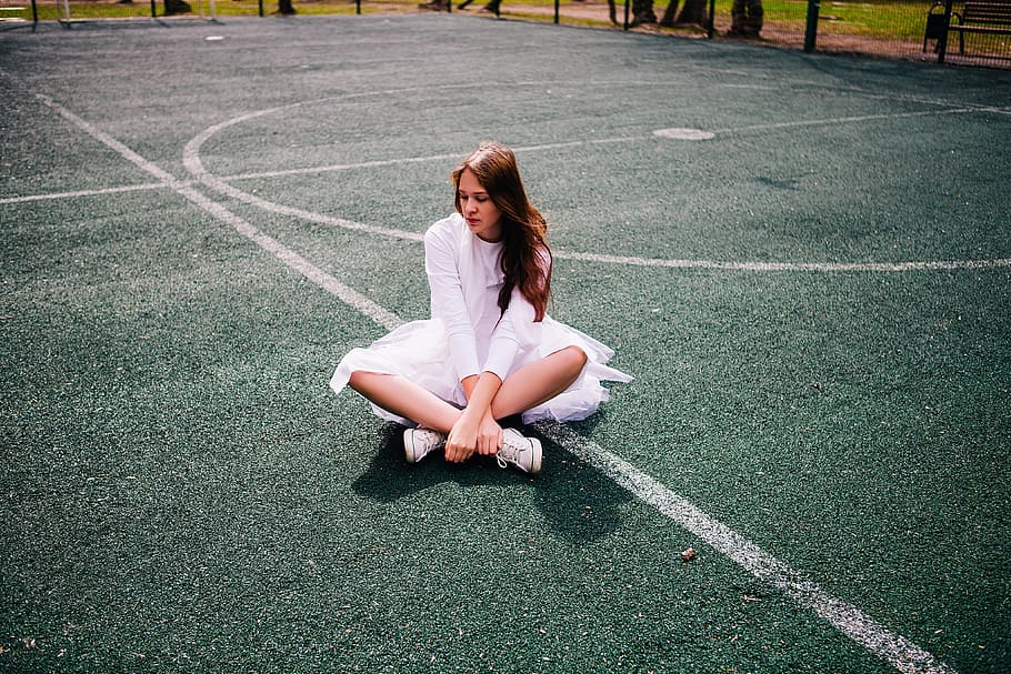 woman wearing white dress sitting on basketball court during daytime