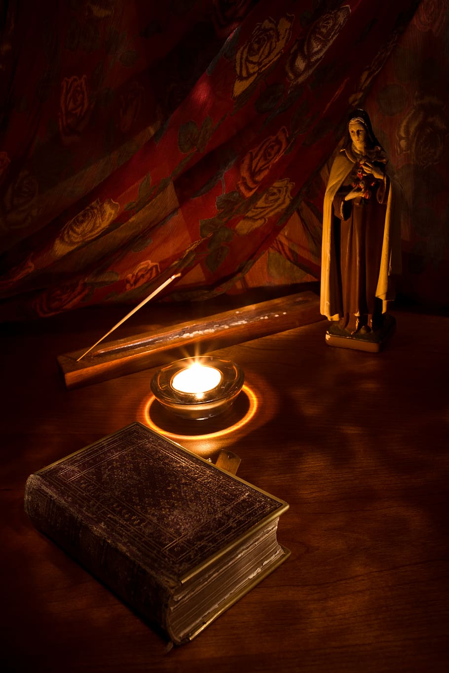 religious figurine near lighted candle and book on brown table