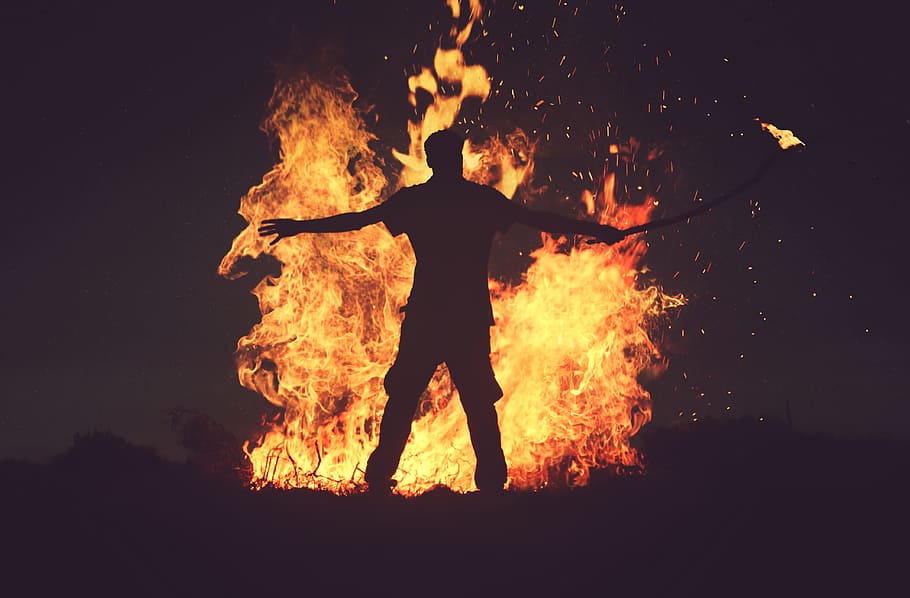 person standing in front of fire during night time, man holding torch in front of bonfire