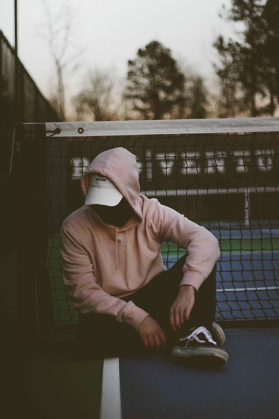 man wearing brown hoodie sitting near tennis net, man in pink hoodie sitting near net