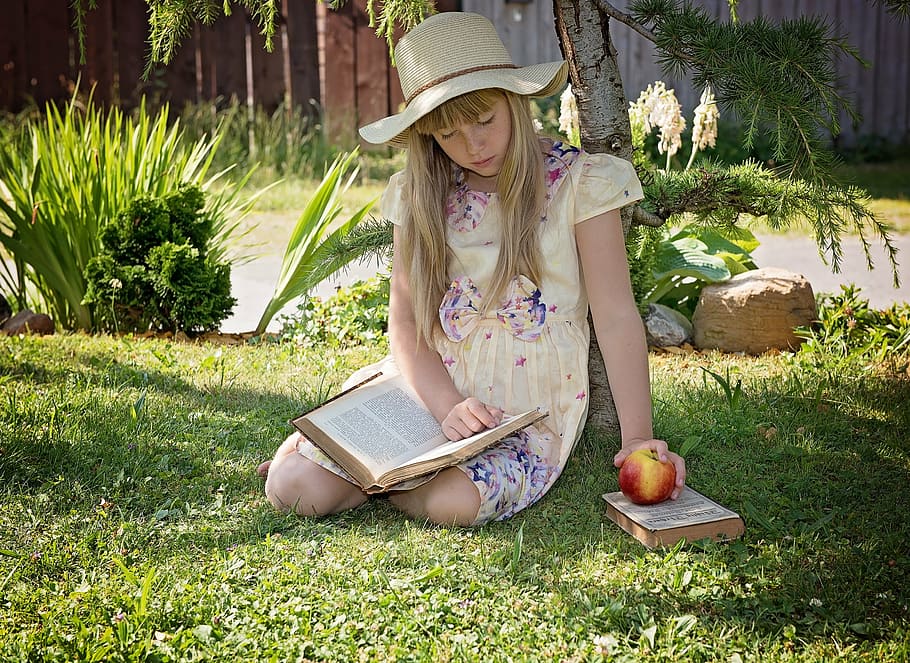 girl wearing dress sitting on grass holding apple and reading book HD wallpaper