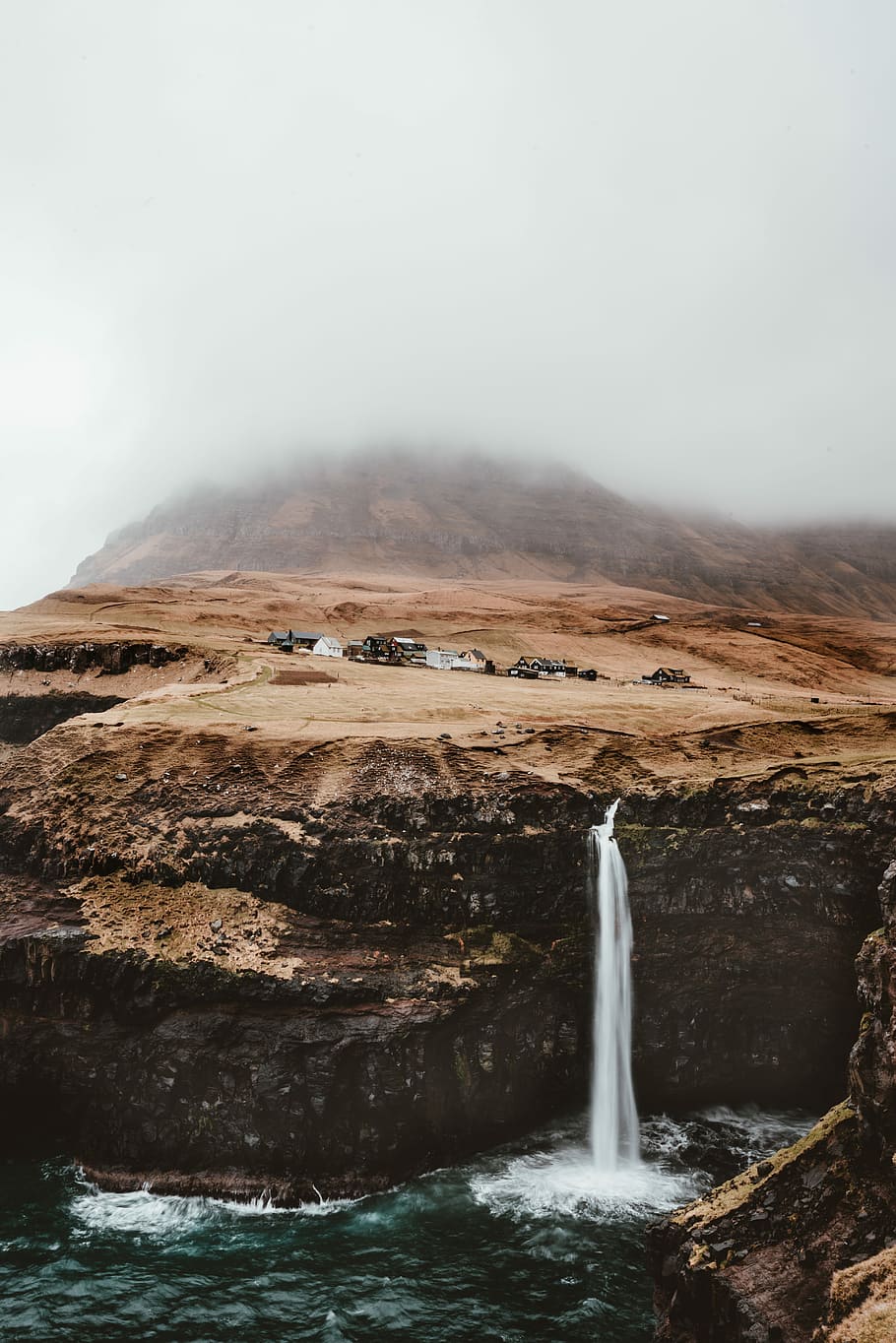 brown mountain with waterfalls under gray cloudy sky, waterfalls near houses HD wallpaper
