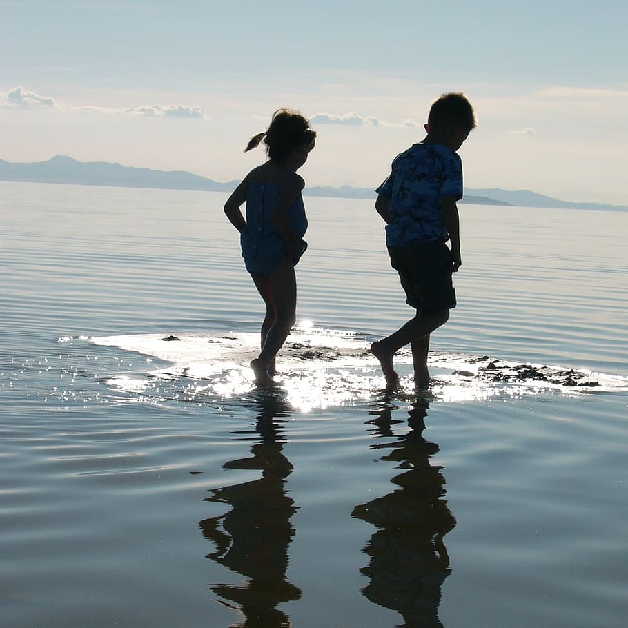 boy and girl walking on the water during daytime, children, river