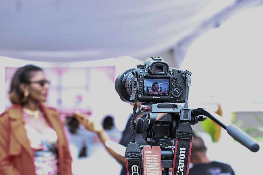 selective focus photo of Canon EOS camera pointed at woman in brown coat HD wallpaper