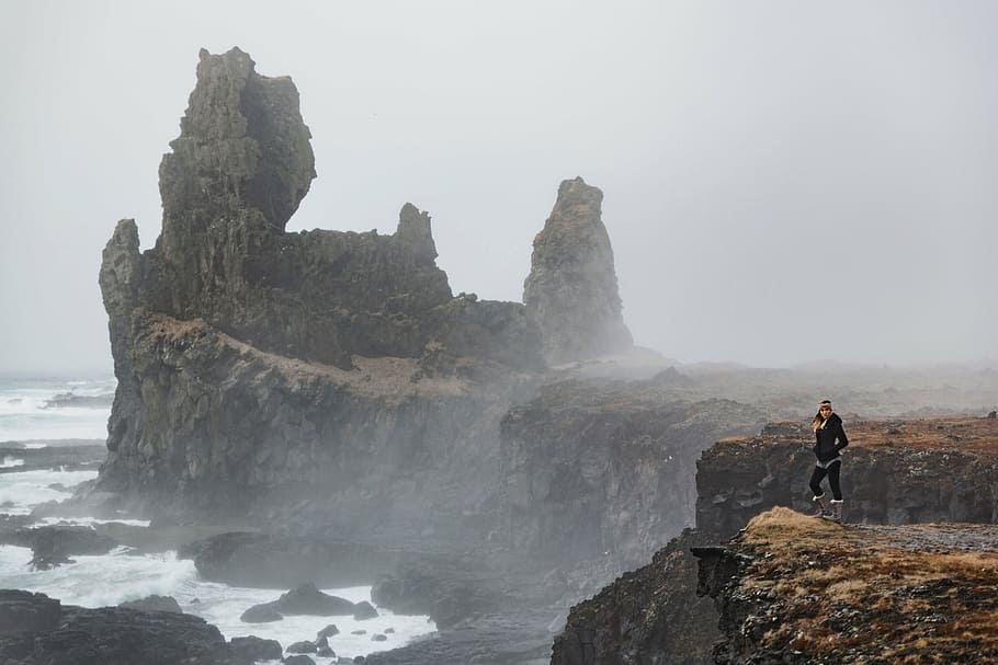 woman in black jacket standing on cliff beside sea, rocks, hill HD wallpaper