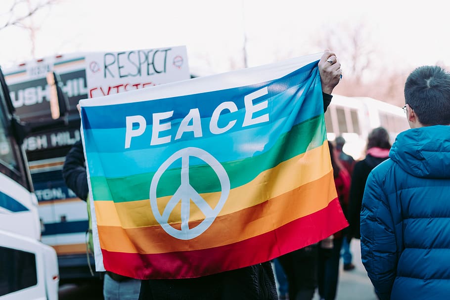 person holding peace flag, person holding rainbow flag with peace symbol in a gathering outside, HD wallpaper