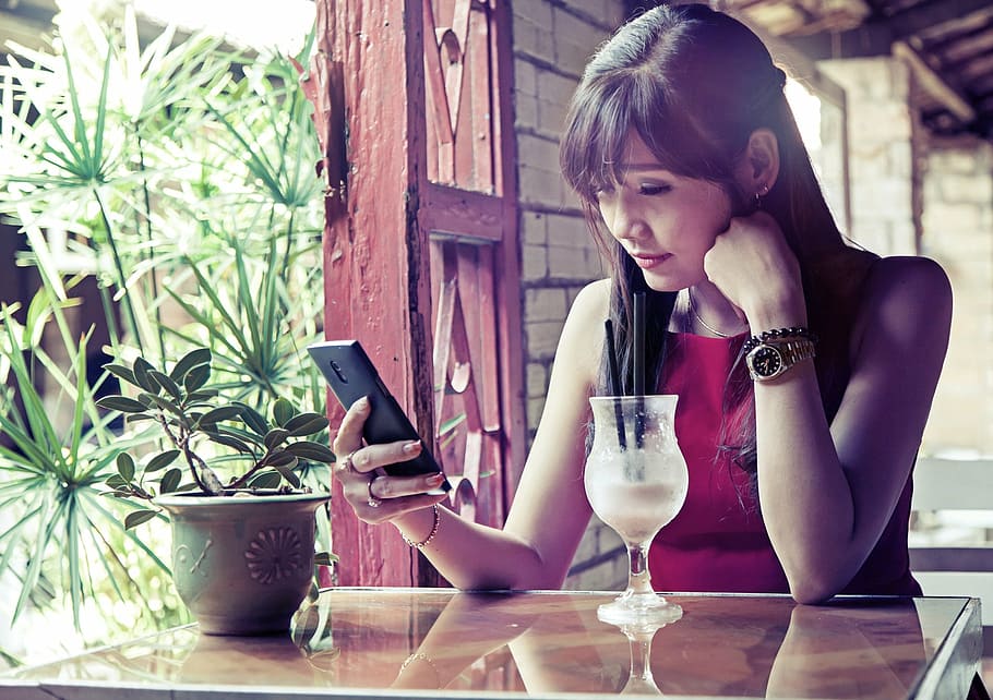 woman wearing red sleeveless top using smartphone while sitting near table, HD wallpaper