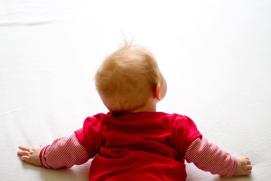 baby wearing red long-sleeved shirt laying on white surface HD wallpaper