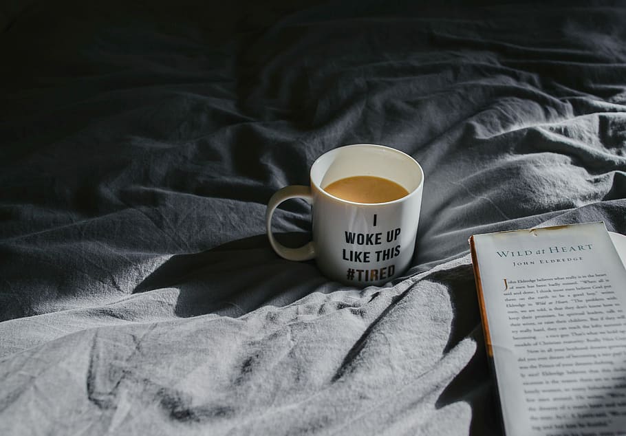 white and black ceramic mug filled with brown beverage on gray textile near Wild at Hearts book, white mug filled with coffee beside book, HD wallpaper