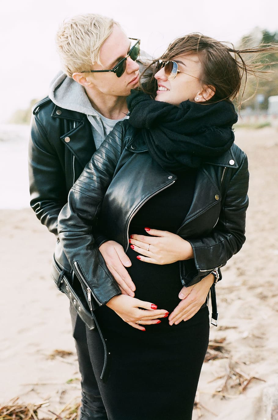 Man in Black Leather Zip Jacket Hugging Woman in Black Leather Zip Jacket and Black Pants Standing on Sand at Daytime HD wallpaper