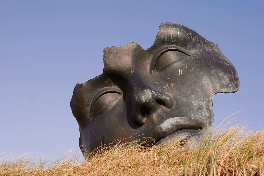 black mask on brown grass under blue skies, face, image, sculpture