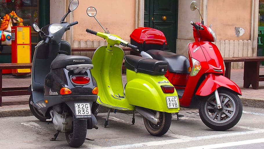 three gray, green, and red motor scooters parked beneath stores